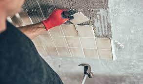 Man removing tile from wall wearing safety gloves