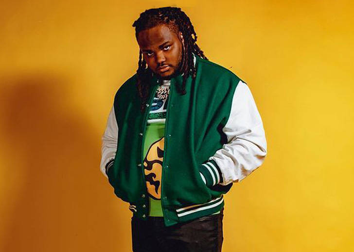 tee grizzley wearing a green and white jacket standing in a yellow background