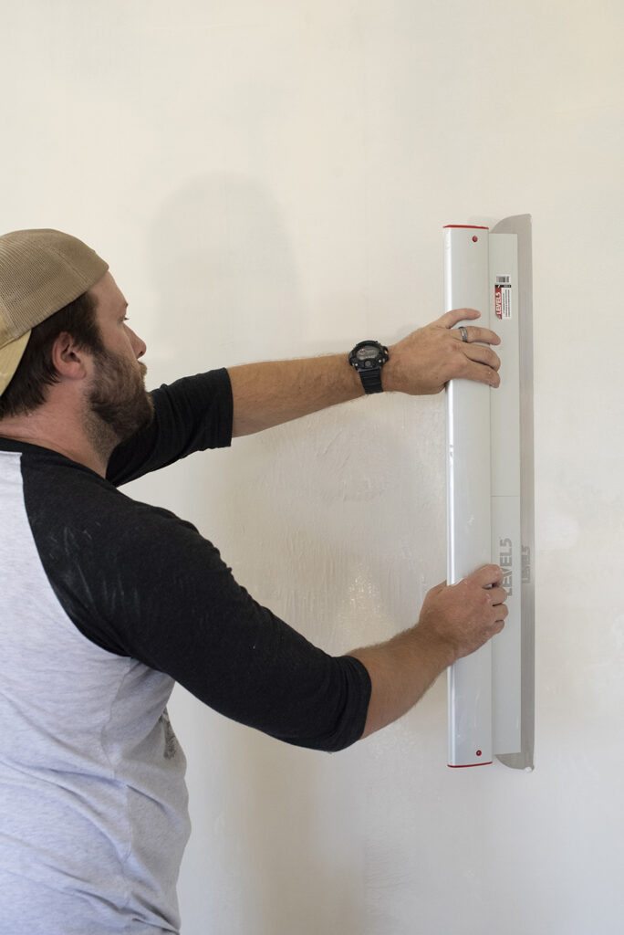 man using leveling tool to skim coat the wall