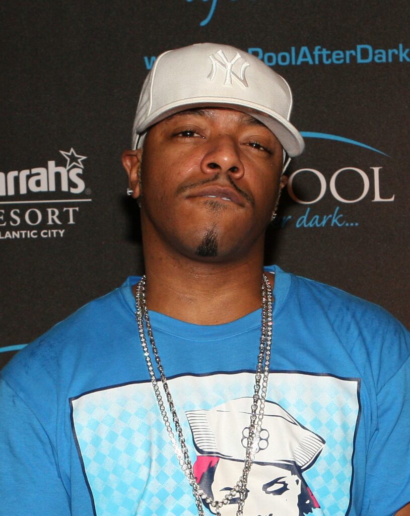 Sisqo wearing a white face cap and silver chains around his neck