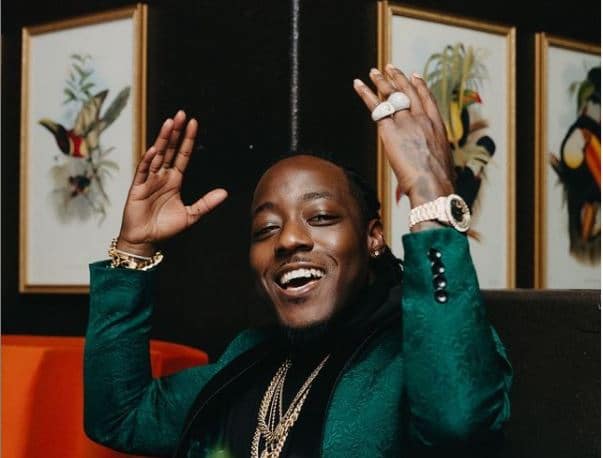 Ace Hood on a green suit and smiling with his hands up