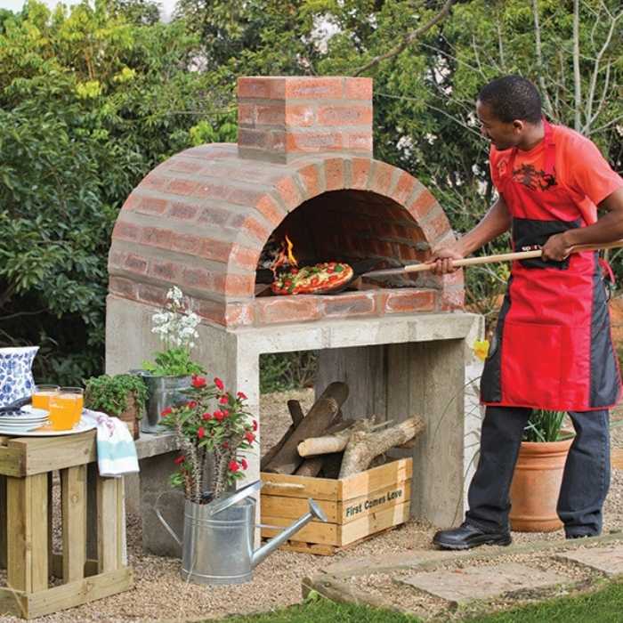 a man baking pizza from an outdoor fireplace with pizza oven
