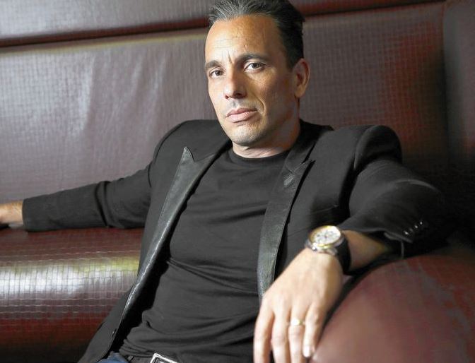 Sebastian Maniscalco sitting on a chair wearing a black suit