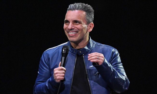 Sebastian Maniscalco performing on stage and holding a microphone